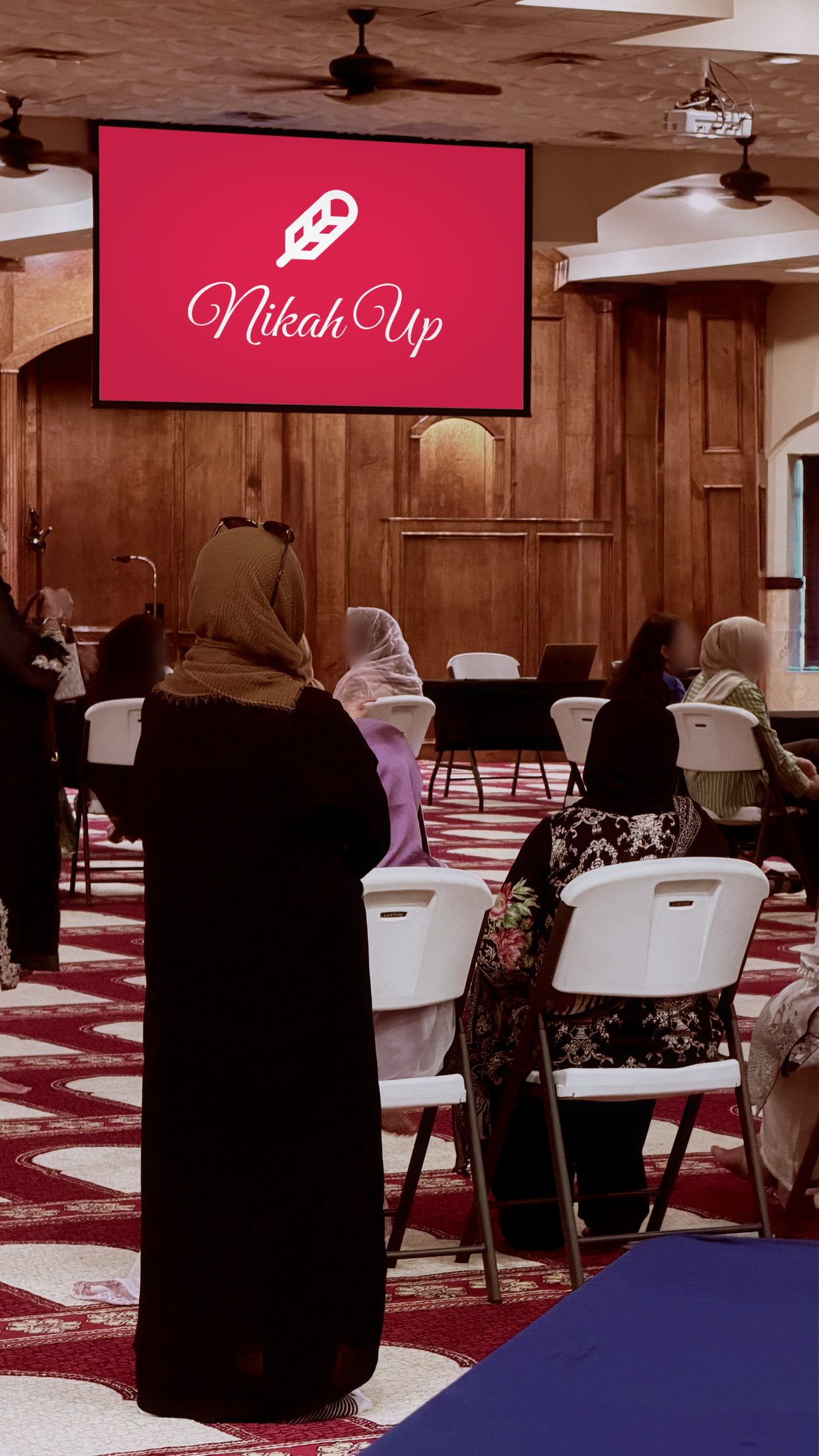 The women’s seating at the front of the hall, the NikahUp screen above the wood panelling.